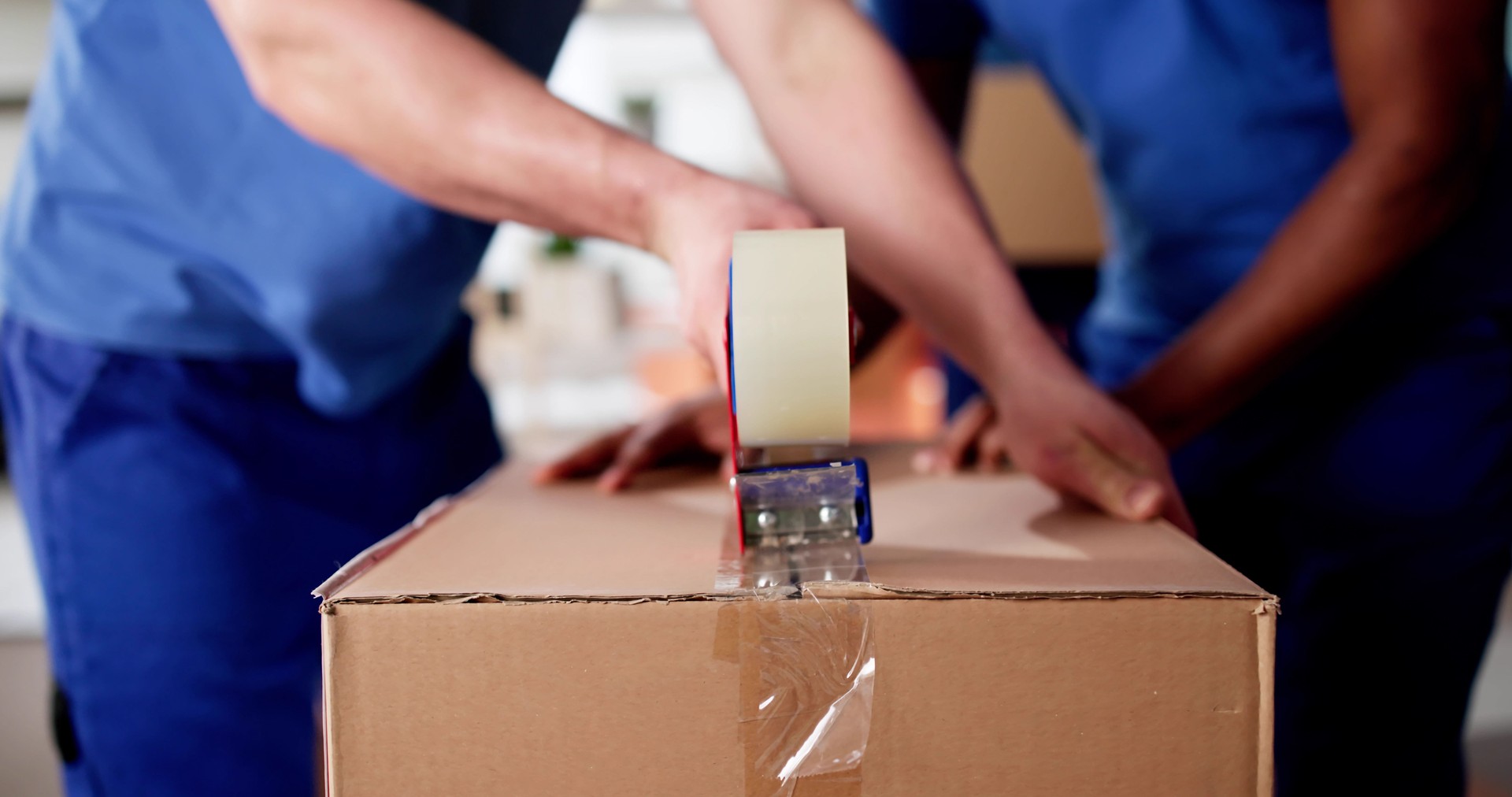 Professional Movers Pack Cardboard Boxes With Tape to Relocate Furniture