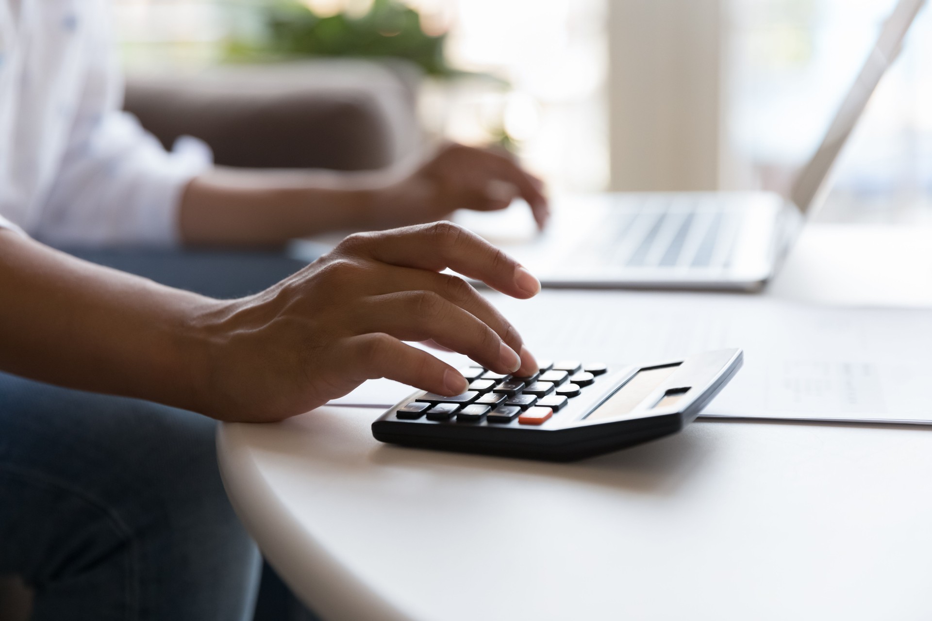 Woman uses calculator and laptop seated at table, close up