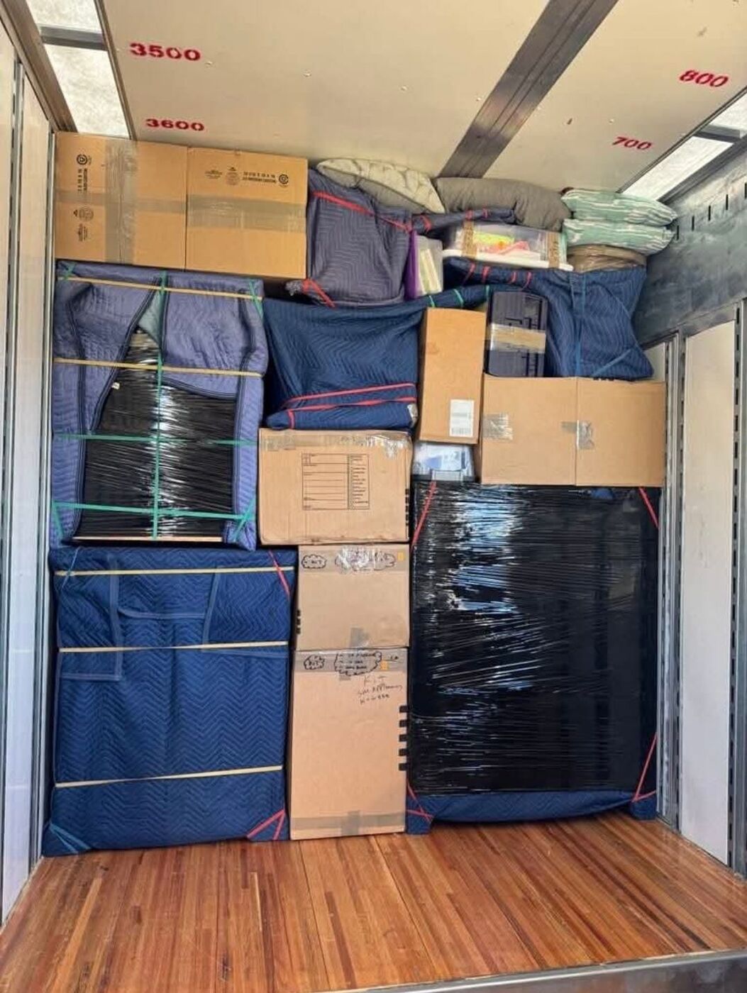 Fully packed moving truck interior with blue blanket-wrapped frames, plastic-wrapped furniture and secured boxes — One World Van Lines Irving, TX DFW movers