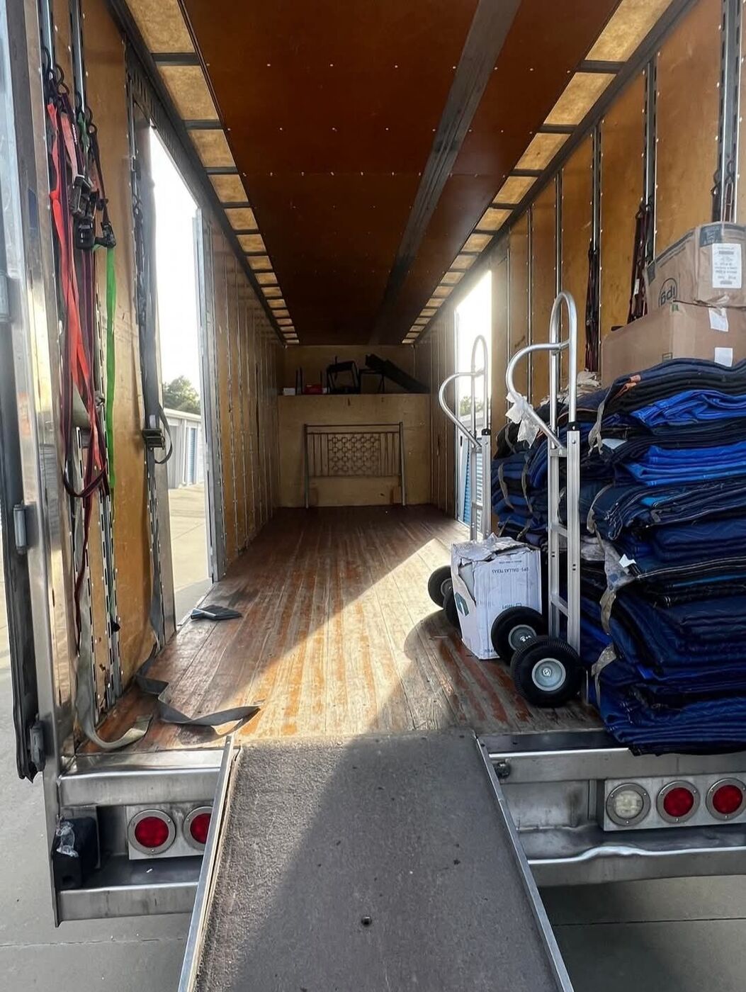 Large moving truck interior with ramp deployed, hand-truck dolly, and stacked blue moving blankets ready for a job — One World Van Lines Carrollton, TX