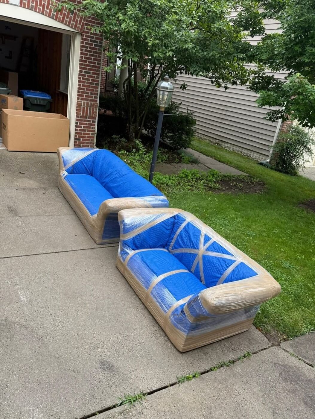 Two sofas wrapped in plastic and moving blankets on a residential driveway — DFW furniture protection